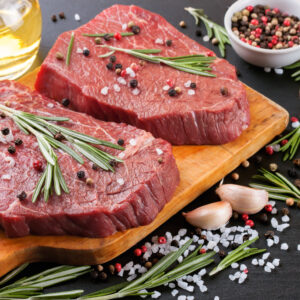 Raw beef steak with spices and ingredients for cooking on cutting borard and slate background.